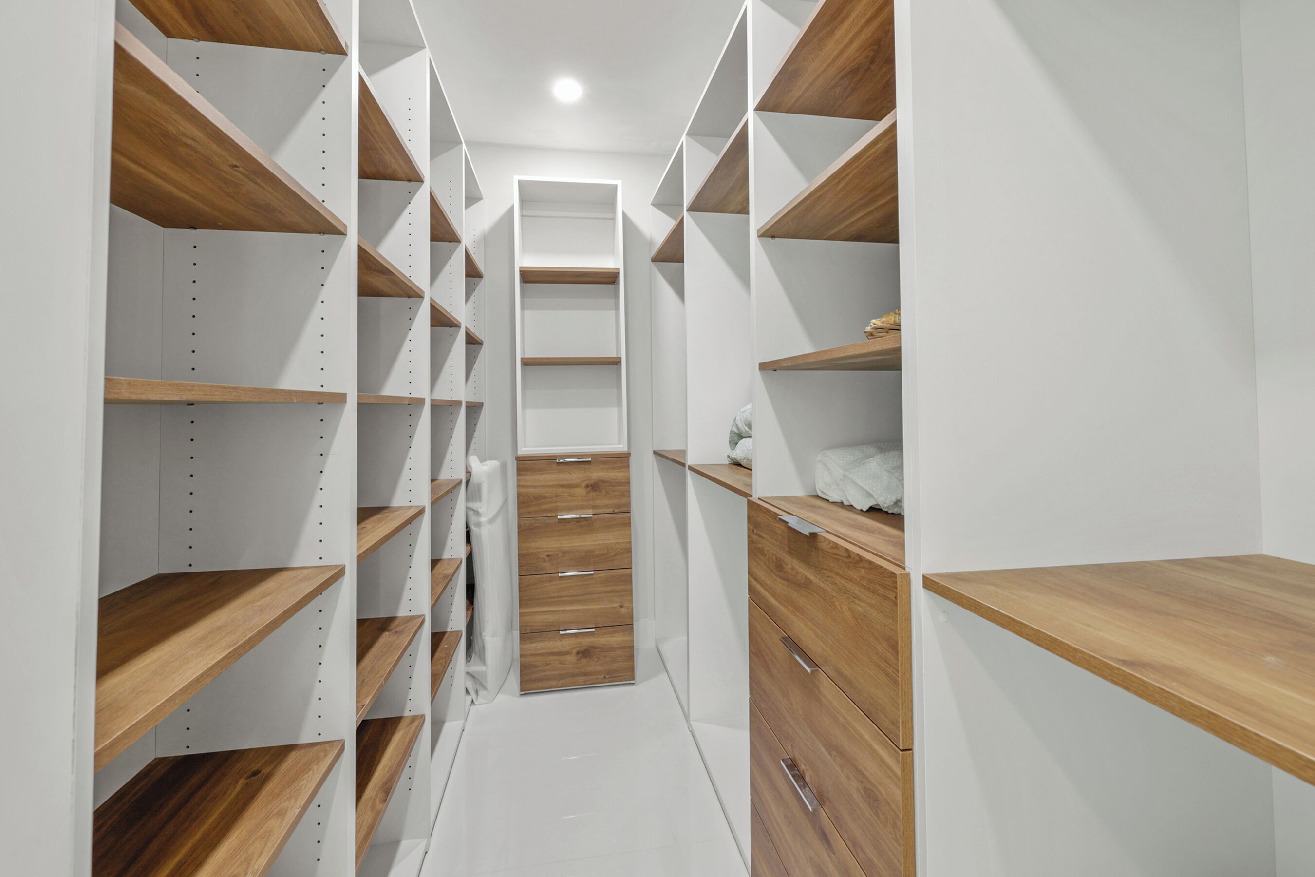 Un petit dressing étroit avec des étagères et des tiroirs en bois, doté d’une porte coulissante centrale.