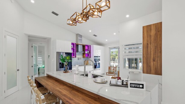 A modern kitchen with a marble countertop, wooden bar seating, and a coffee station. - Waterfront Gulf Access Paradise in Marco Island – Pool, Jacuzzi & Game Room Fun! (Marco Island)