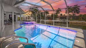 A modern indoor swimming pool with clear glass ceilings, surrounded by palm trees and a sunset view. - Waterfront Gulf Access Paradise in Marco Island – Pool, Jacuzzi & Game Room Fun! (Marco Island)