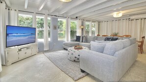 A living room with a television, grey sofa, ottoman, and a white cabinet. - Pelicans Landing - 4BR/3BA Home - Heated Pool - - Close to Beach and Historic Downtown (Stuart)