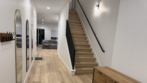 Un interior moderno con una escalera de madera, un banco y un pasillo que conduce a una sala de estar con un sofá y una mesa de centro.