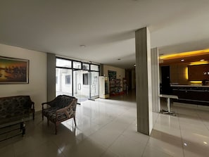 Un hall espacioso con una moderna recepción, un área de descanso con mobiliario estampado y vistas al exterior a través de grandes puertas de vidrio.