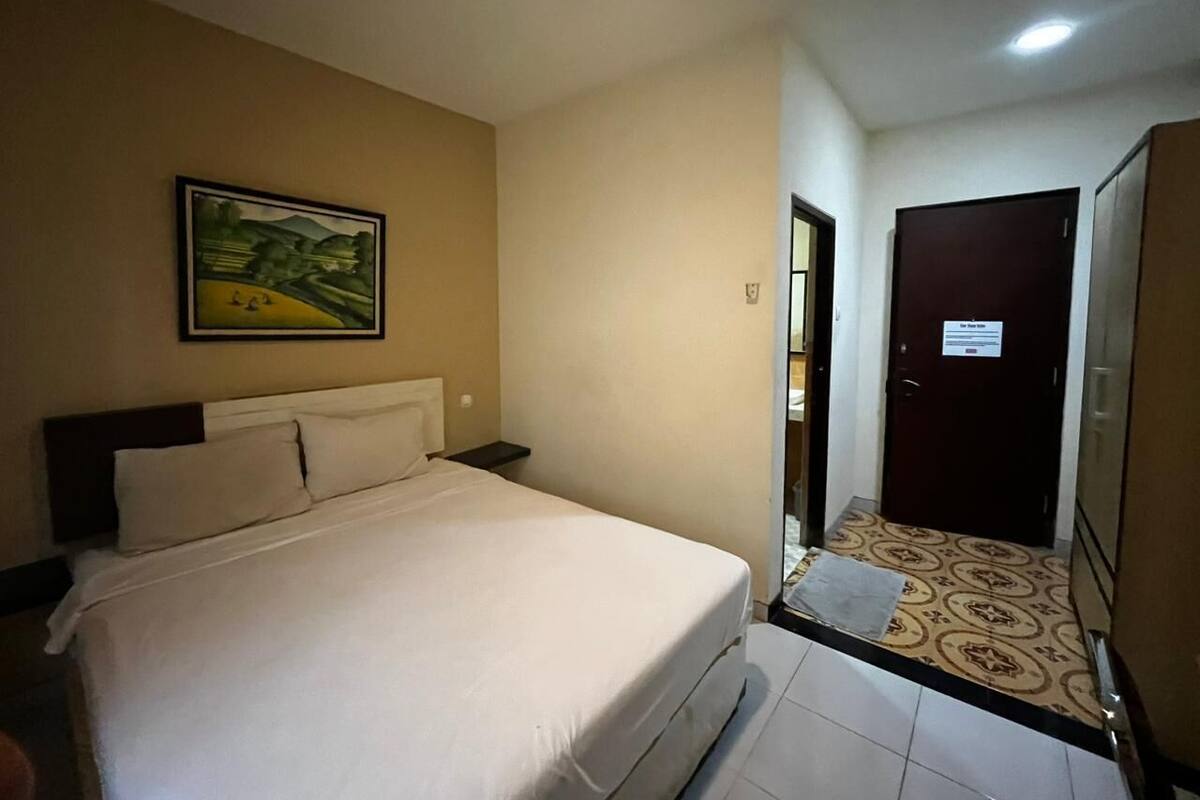 A hotel room with a bed, a painting on the wall, a door, and a patterned floor.