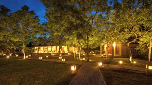 Area esterna illuminata di notte, con vialetto lastricato, alberi e lanterne.