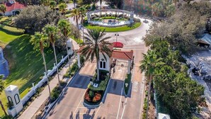 Vista aèria d'una urbanització tancada amb una plaça circular central, palmeres i una carretera que condueix a una entrada tancada.