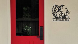 A red door with a window, a 'Hello' mat, and a logo for 'Airstream Retreat' on the wall. - Ai's Rural Retreat 2 (Motueka)