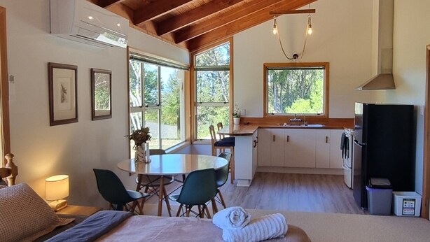 A room with a wooden ceiling, a bed, a dining table, chairs, a TV, and a window with a view of trees. - Ai's Rural Retreat 2 (Motueka)