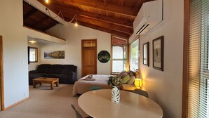 A cozy living room with a sofa, a coffee table, and a dining table. There is a door leading to another room, a painting on the wall, and a window with blinds. - Ai's Rural Retreat 2 (Motueka)