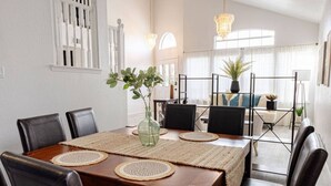 Un comedor con una mesa de madera, sillas negras, individuales tejidas y un florero con plantas verdes.