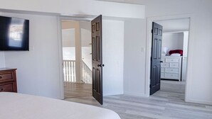 Un dormitorio con cama, cómoda y televisor montado en la pared. Hay dos puertas que dan a otras habitaciones.