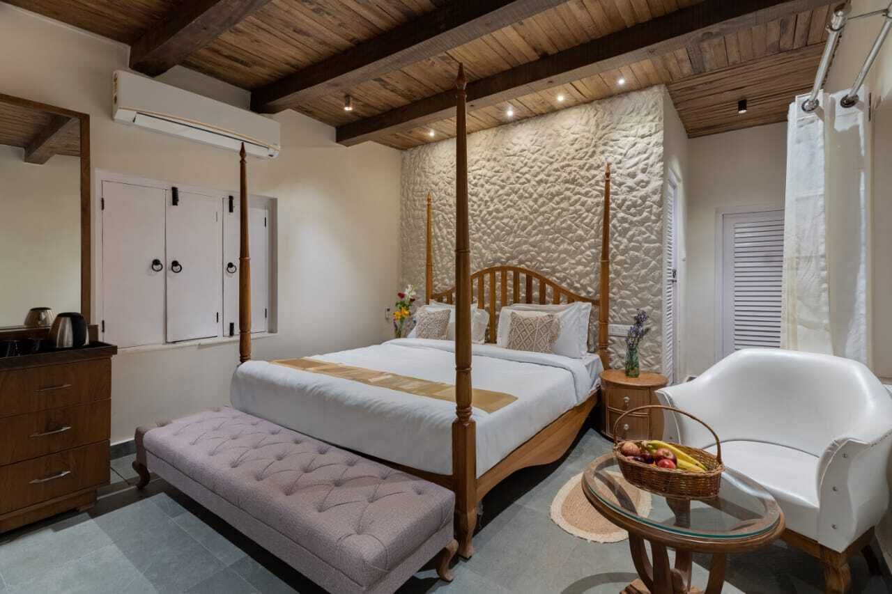 A bedroom with a four-poster bed, a wooden dresser, a bench, a chair, and a small table with fruit.