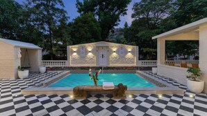 A pool area with a checkered floor, a central bench, and a building with illuminated windows. - AbhiRaj Villa (Udaipur)