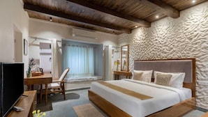 A bedroom with a large bed, wooden headboard, and a stone wall. - AbhiRaj Villa (Udaipur)