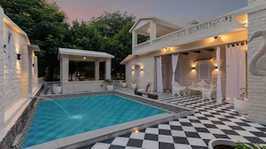 A pool area with a checkered floor, white outdoor furniture, and a covered seating area. - AbhiRaj Villa (Udaipur)