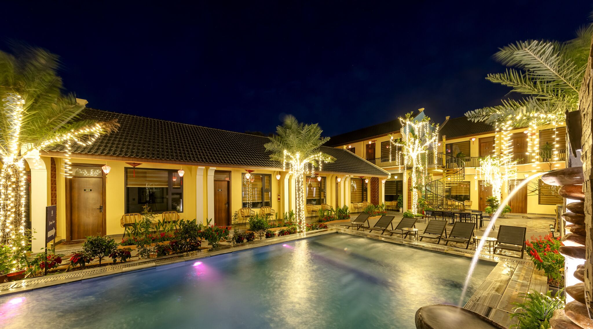 A hotel with a swimming pool, outdoor seating, and decorative lights.