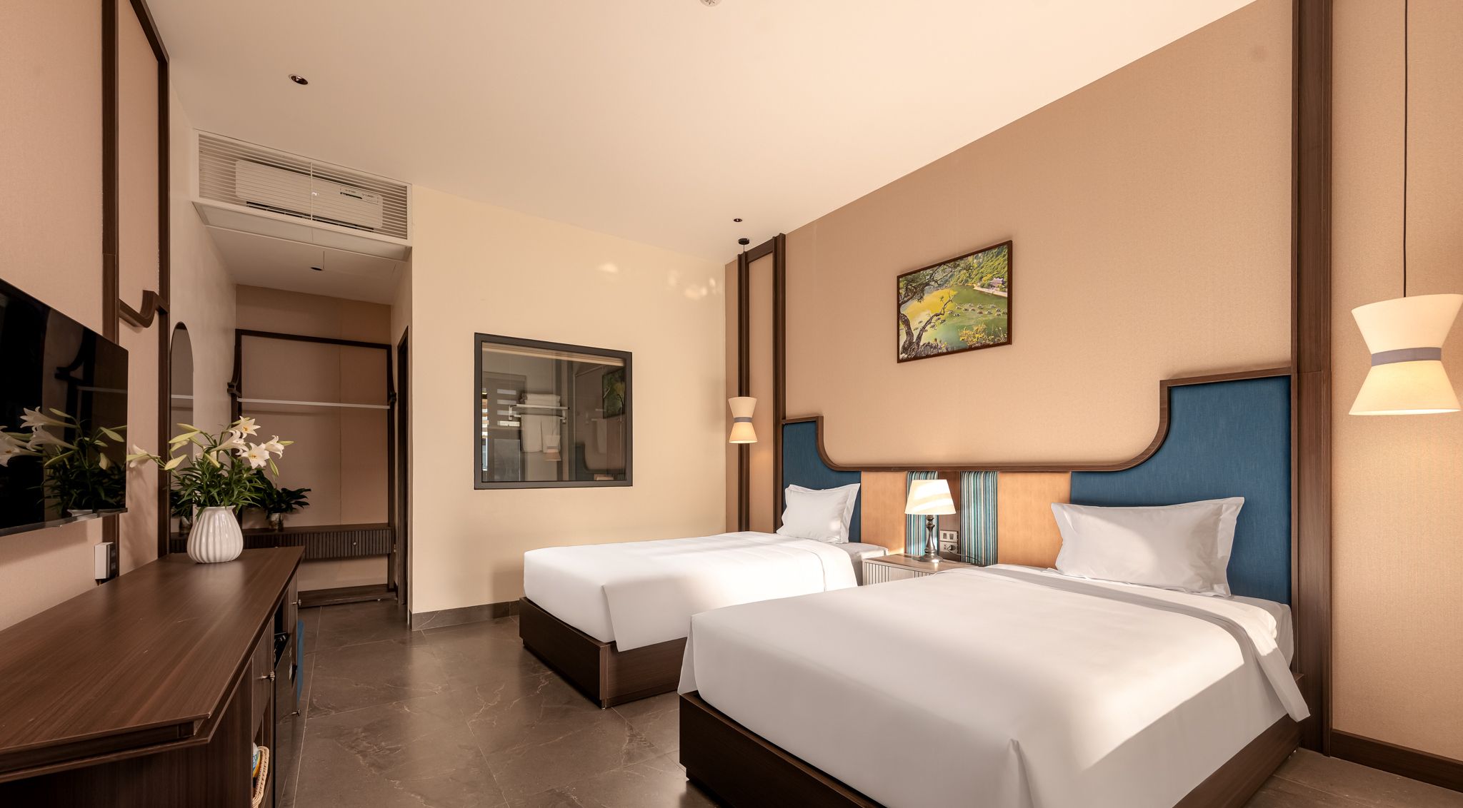 Habitación de hotel con dos camas, un escritorio, un espejo, un cuadro y un aire acondicionado de pared.