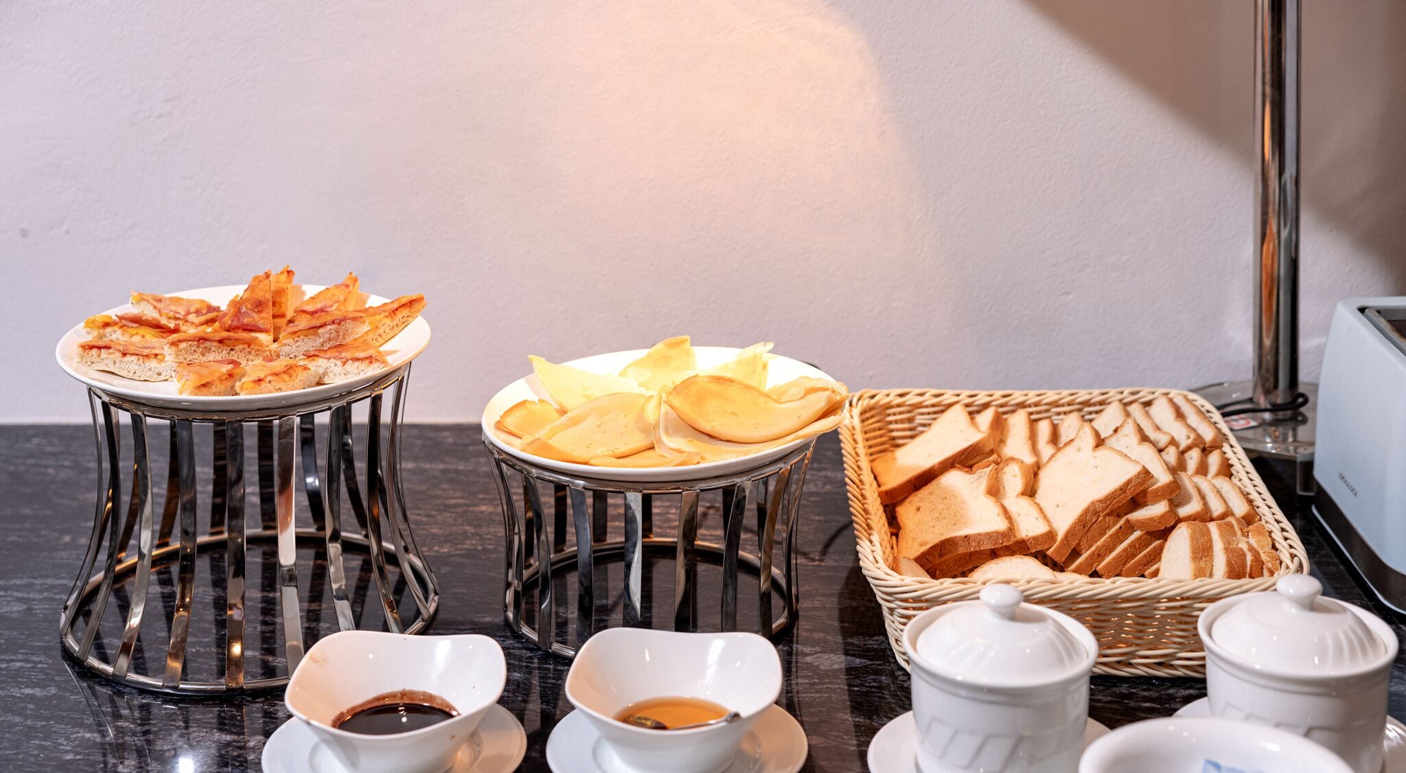 Desayuno con una fuente de cruasanes, una fuente de queso y una cesta de pan sobre una encimera de mármol.