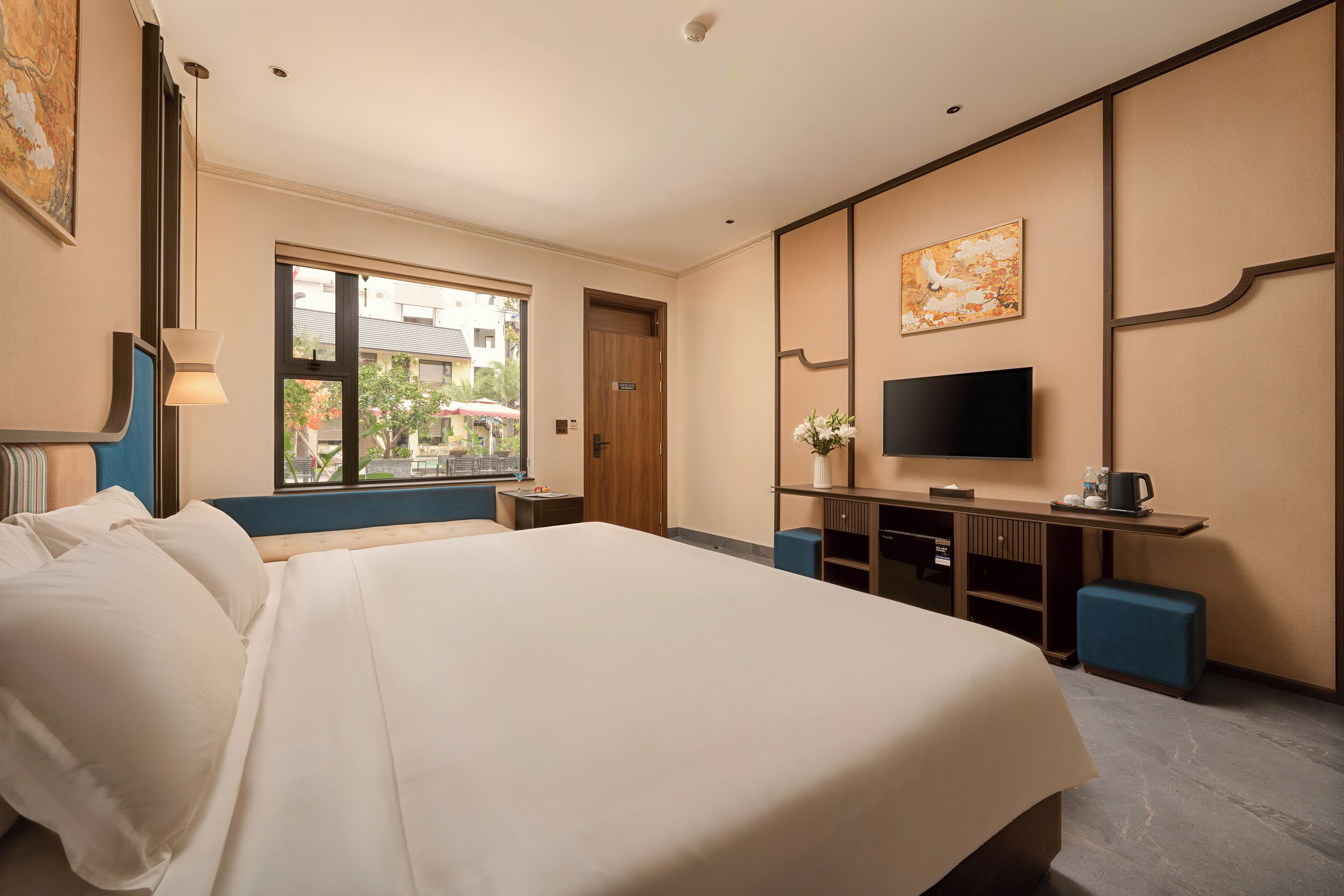 Habitación de hotel con una cama grande, televisión, escritorio con computadora y ventana con vista a edificios.