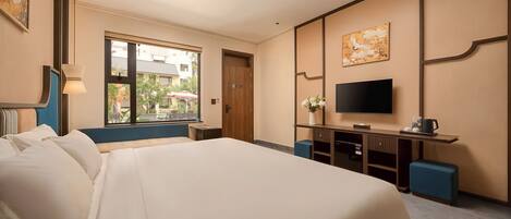 Habitación de hotel con una cama grande, televisión, escritorio con computadora y ventana con vista a edificios.