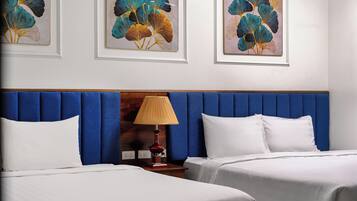 Camera d'albergo con due letti, una testiera blu, una lampada da comodino e opere d'arte incorniciate al muro.