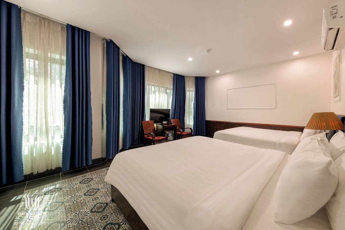 A hotel room with two beds, a desk with a chair, a TV, and a lamp.