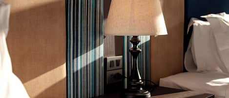 A neatly made bed with white linens, a bedside table with a lamp, and a striped curtain.