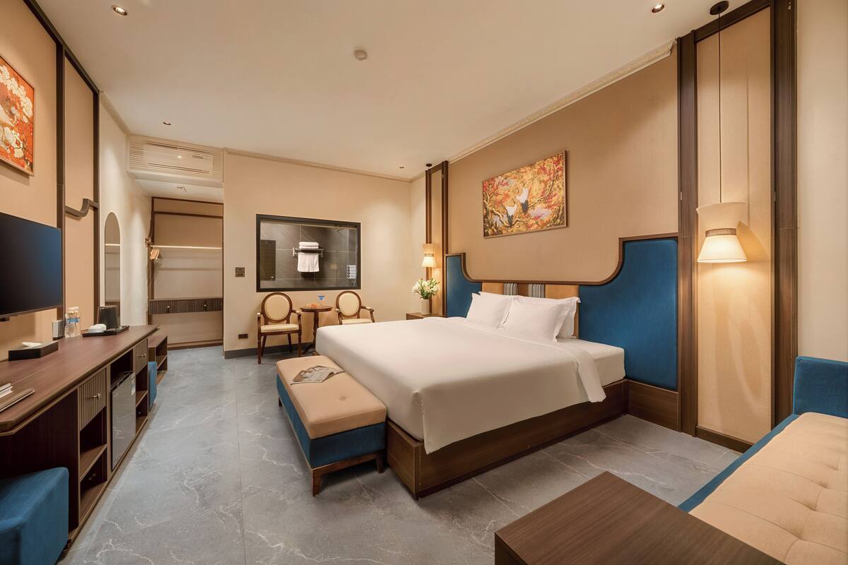 A hotel room with a bed, a desk, a chair, a TV, and a painting on the wall.