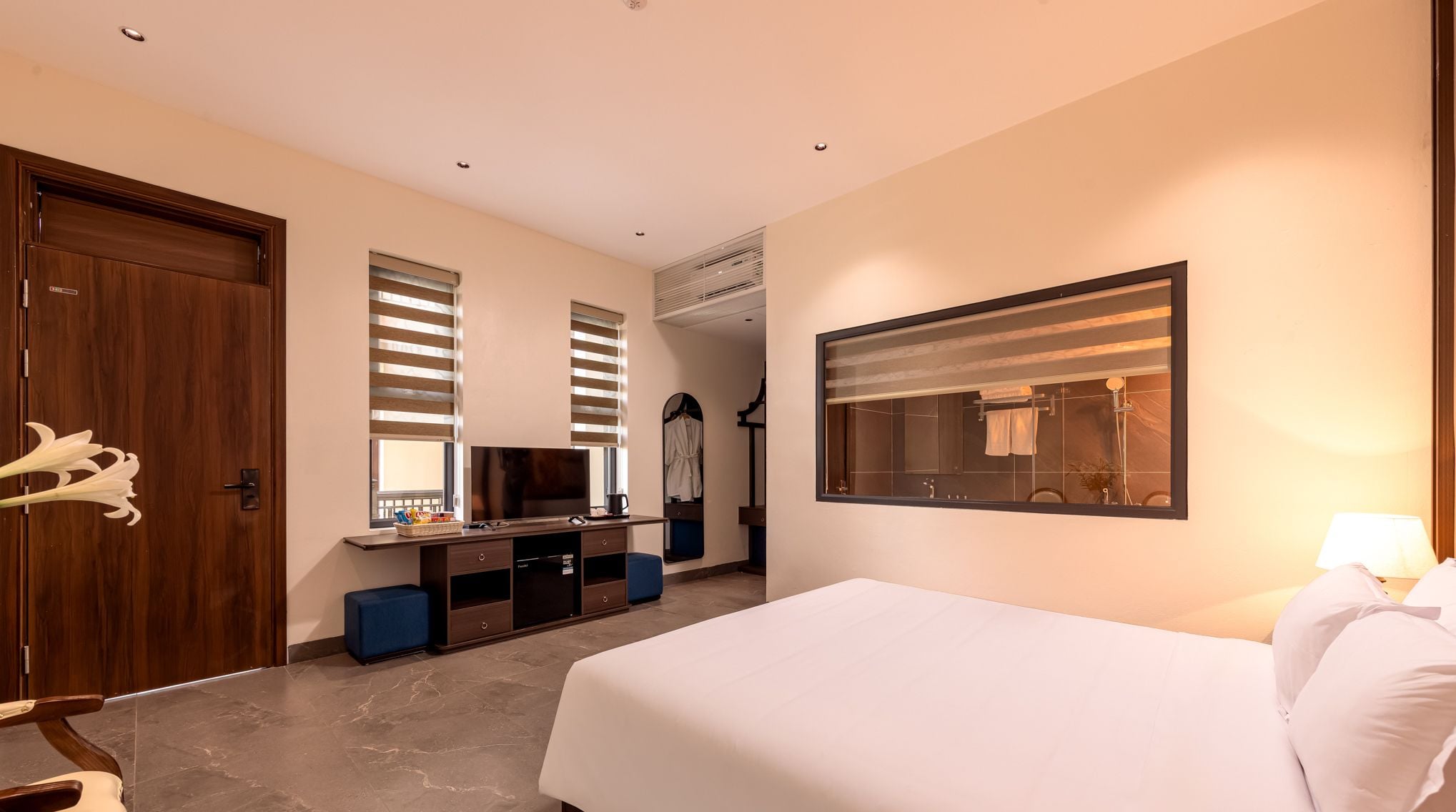 Habitación de hotel con cama, escritorio con televisor, espejo y ventana con persianas.