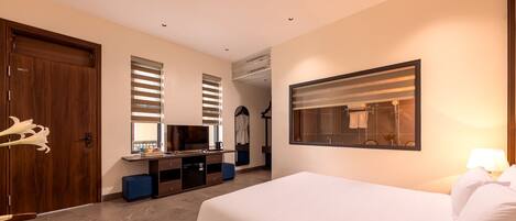 A hotel room with a bed, a desk with a TV, a mirror, and a window with blinds.