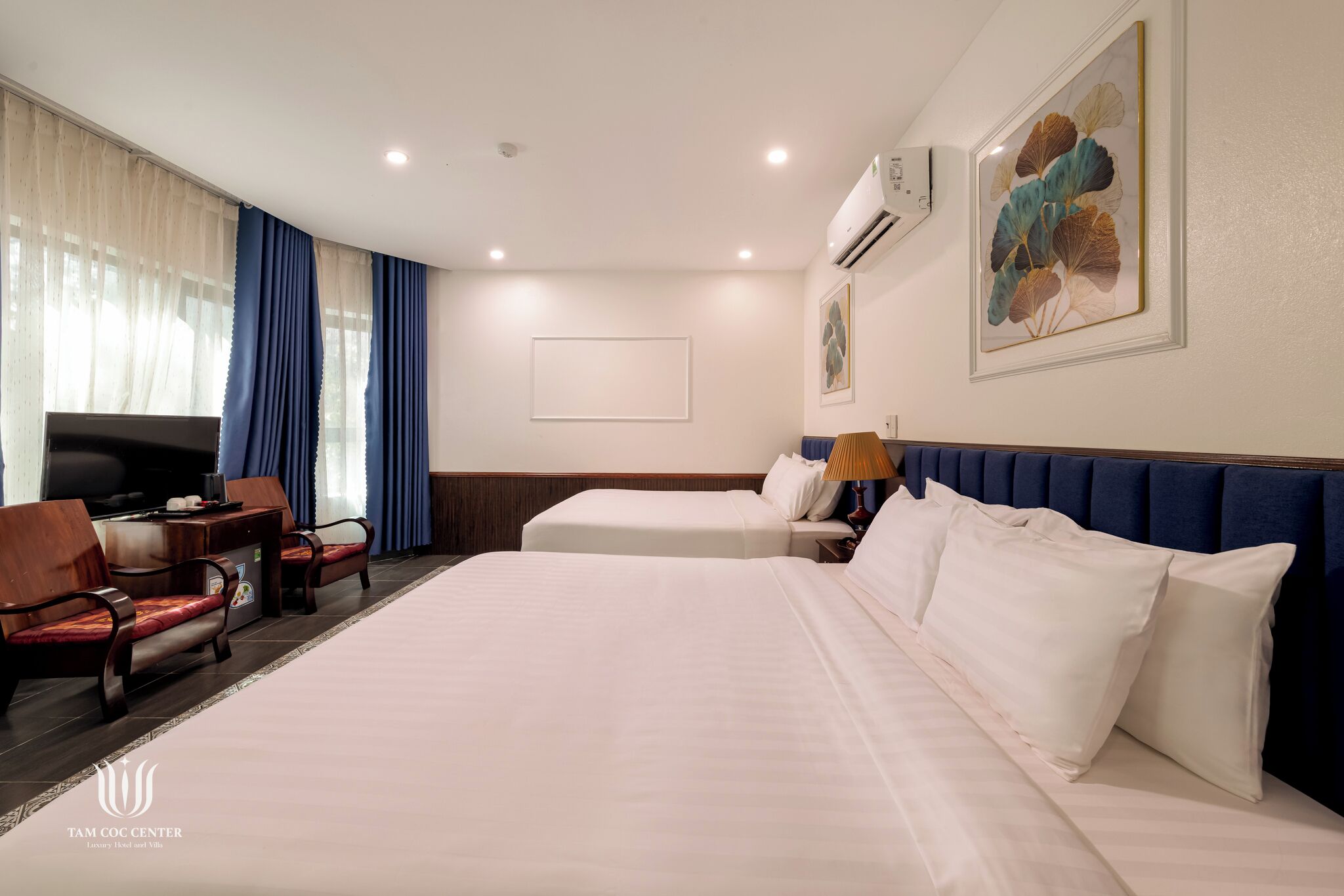 Une chambre d’hôtel avec un grand lit, deux tables de chevet, un bureau avec une chaise, une télévision et une fenêtre avec des rideaux.