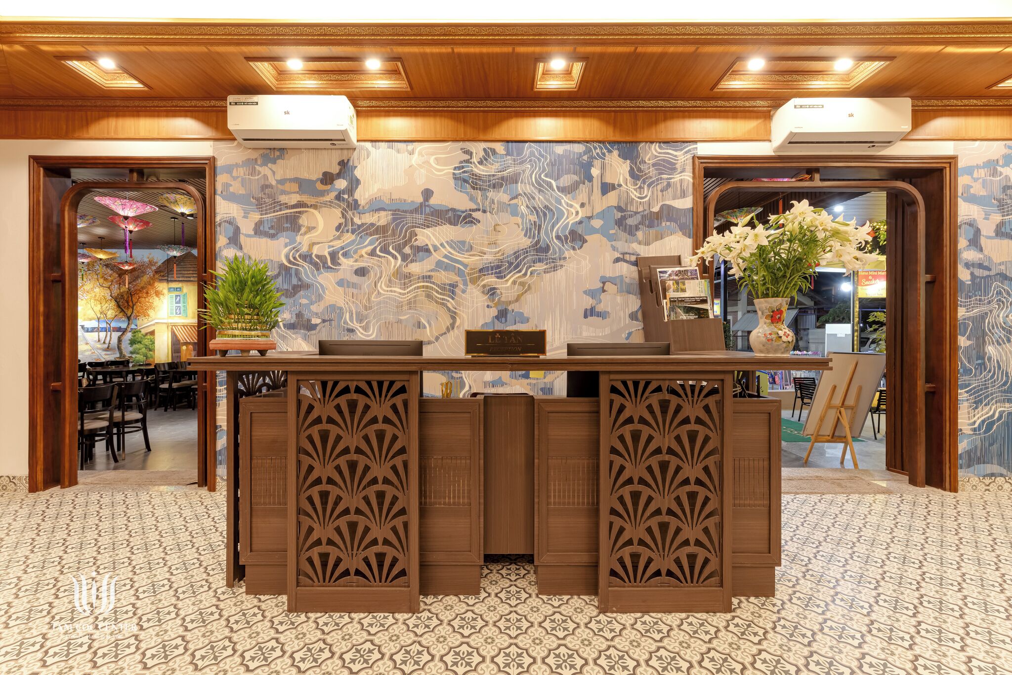 A reception desk with intricate woodwork, a patterned floor, and a decorative wall mural.