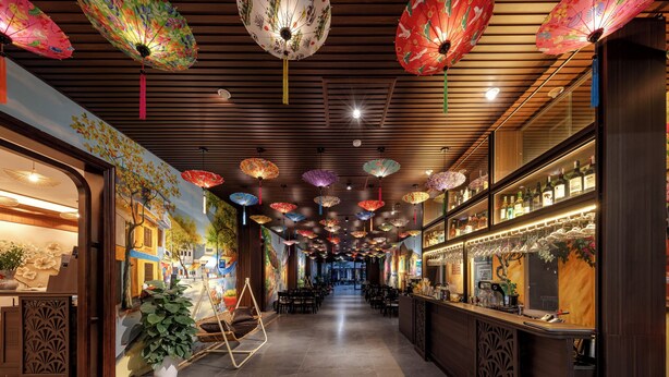 Un pasillo con techo de madera, paraguas decorativos colgantes y una zona de bar con estantes llenos de botellas.