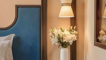 Et hotelværelse med en seng, et natbord med en vase med blomster og en vægmonteret lampe.