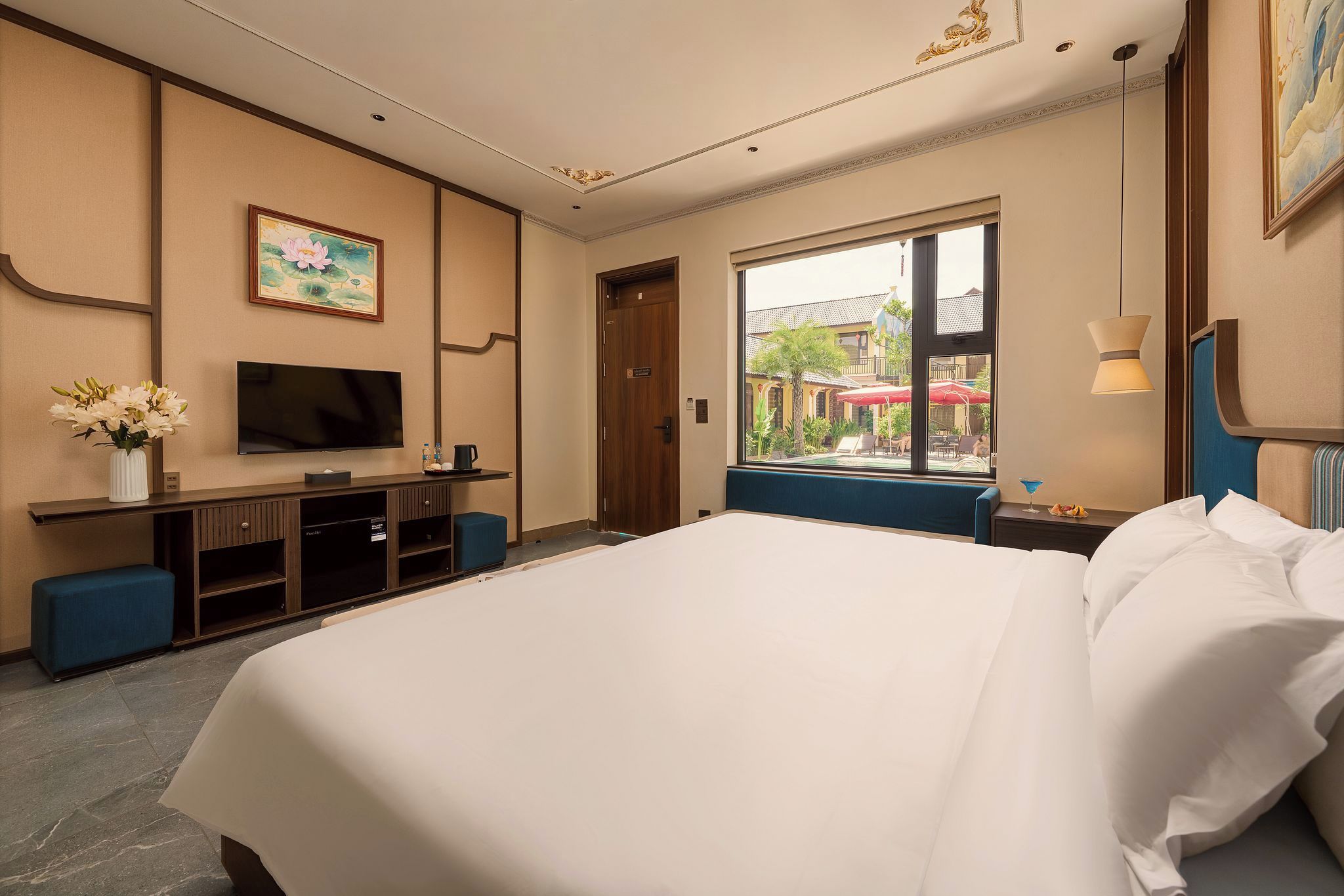 Ein Hotelzimmer mit einem großen Bett, einem Fernseher, einem Schreibtisch mit Blumenvase und einem Fenster mit Blick nach draußen.