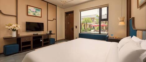 A hotel room with a large bed, a television, a desk with a vase of flowers, and a window with a view of the outside.