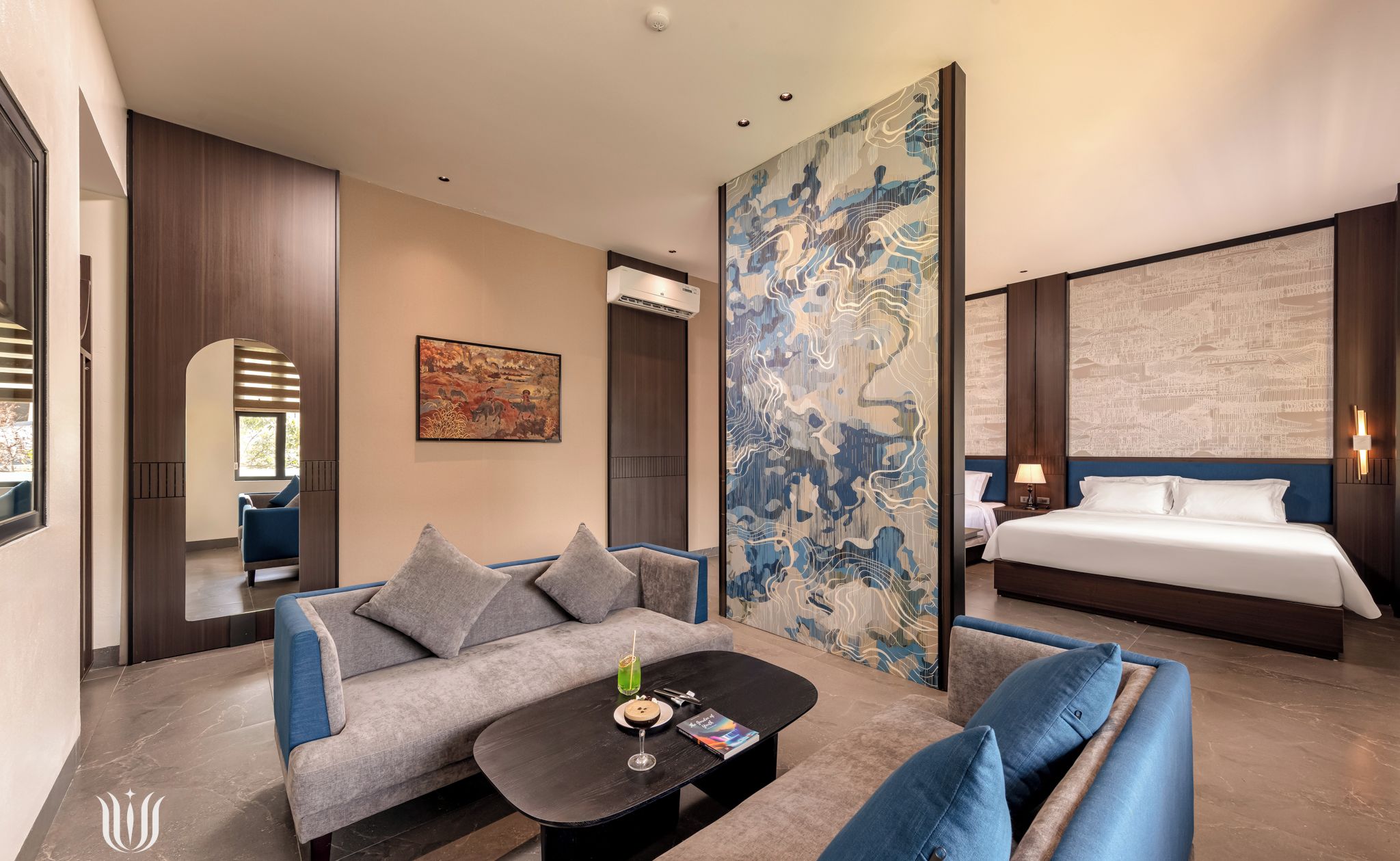 Une chambre d’hôtel moderne, dotée d’un canapé, d’une table basse, d’un lit et d’un grand tableau abstrait accroché au mur.