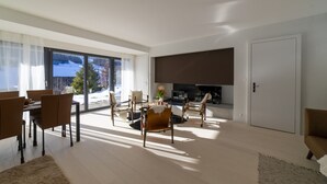 Una sala de estar moderna con comedor, chimenea y ventanas amplias con vista a un paisaje nevado.