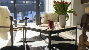 Una mesa con un jarrón de tulipanes, una vela y un vaso de agua junto a una ventana con vistas nevadas.
