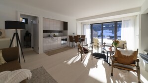 Una sala moderna con sofá, una mesa de comedor y sillas, una cocina con armarios, y un ventanal con vistas.
