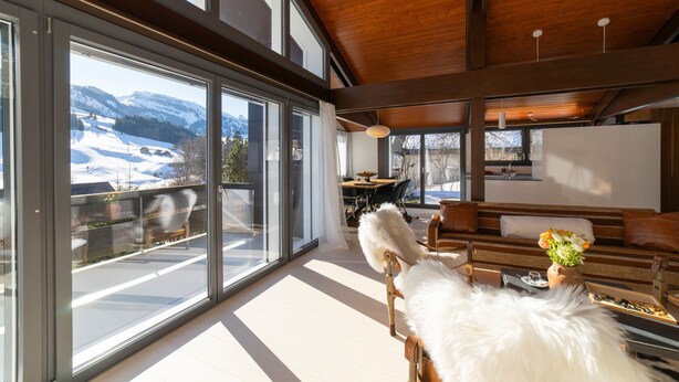 A spacious room with large windows, a wooden ceiling, and a view of a snowy landscape.