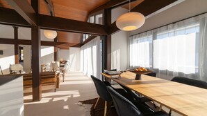 A modern dining area with a long wooden table, black chairs, and a hanging light fixture.