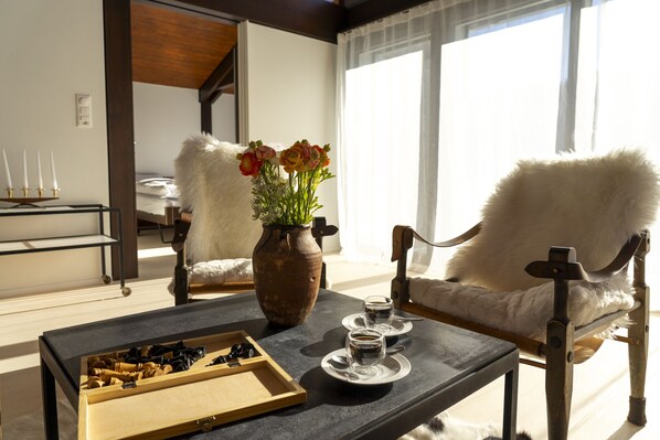 Una habitación con una mesa de madera, un florero con flores, dos sillas y una ventana con cortinas.