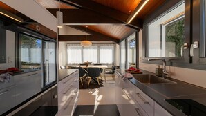A modern kitchen with a dining area, large windows, and a wooden ceiling.