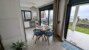 Een eetgedeelte met een ronde tafel voor vier personen, een keuken met moderne apparatuur en uitzicht op de omgeving via grote schuifdeuren.