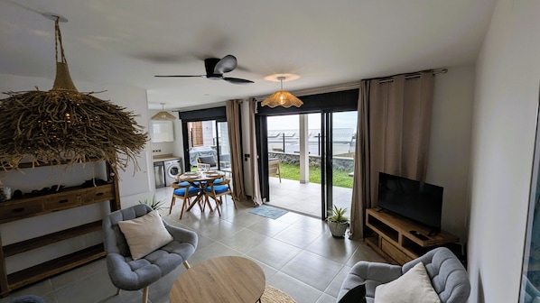 Ett modernt vardagsrum med en soffa, ett soffbord, en tv och en matplats med stolar.