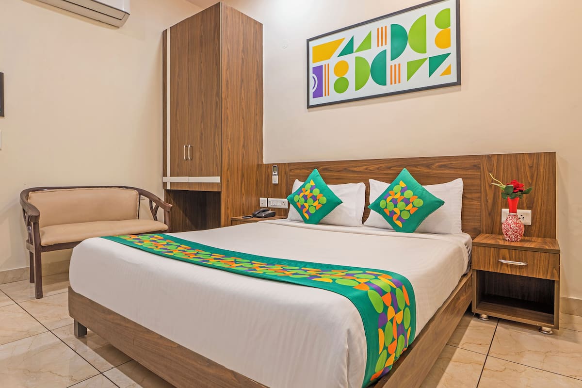 A hotel room with a bed, a chair, a nightstand, a wooden wardrobe, and a wall-mounted artwork.