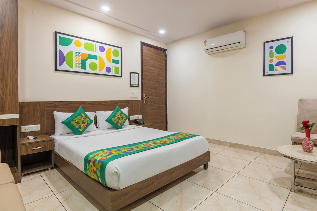 A hotel room with a bed, bedside table, nightstand, chair, small table, and artwork on the walls.