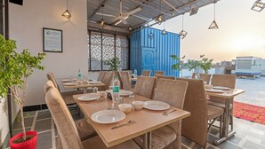 A restaurant with tables set for dining, a blue container in the background, and a sign on the wall. - Treebo Elegant Palace (New Delhi)