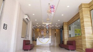 Zona de recepció d'hotel amb taulell de recepció, dos sofàs vermells, una làmpada penjant i una paret decorativa de fusta.