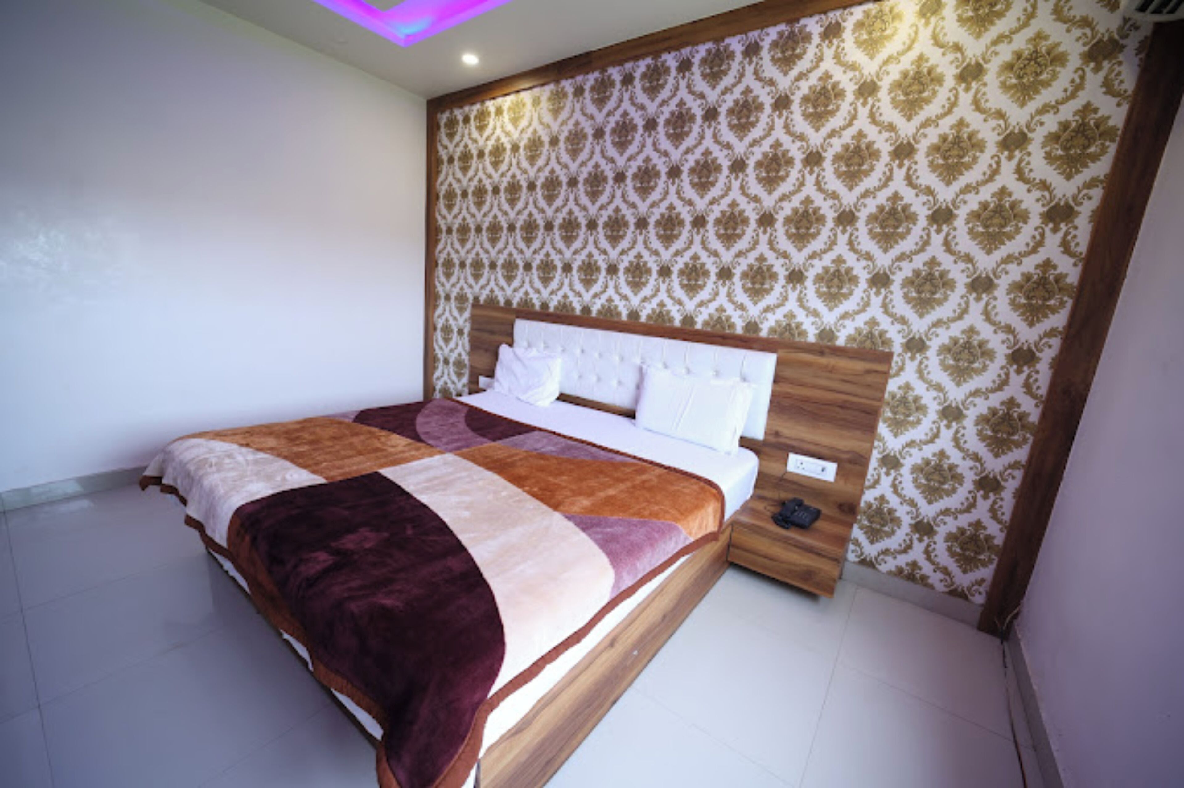 A bedroom with a wooden headboard, patterned wallpaper, and a bed with a multicolored blanket.